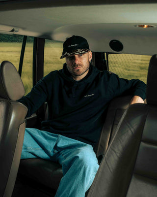 Man sitting in the back seat of a vintage Range Rover, wearing a 6 panel cap with cowhide brim, with a field view outside